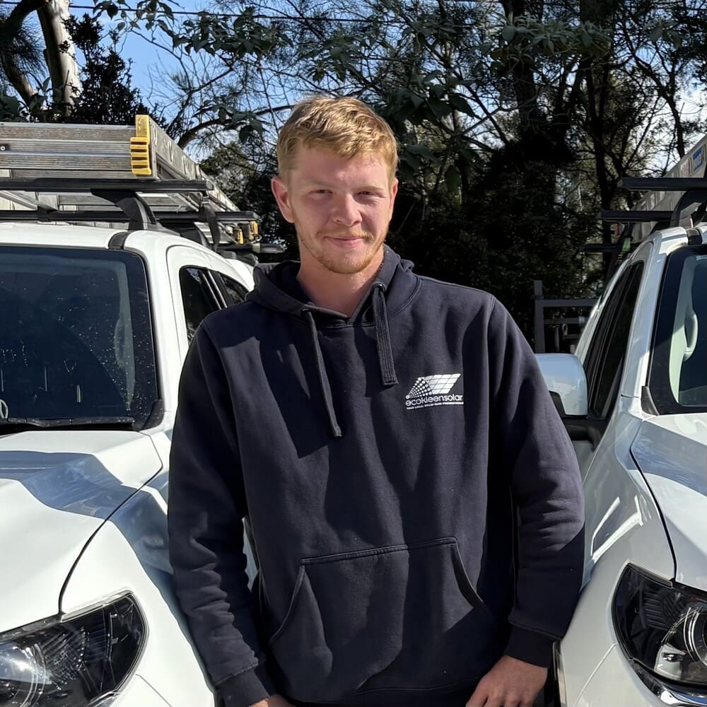Cooper from EcoKleen Solar standing outdoors between two work utes fitted with ladders