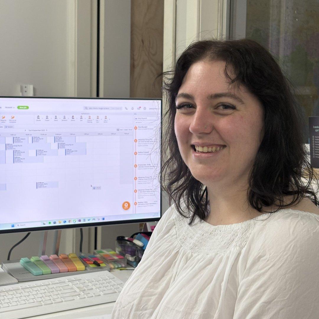 Jess from EcoKleen Solar smiling at her desk with scheduling software open on computer screen